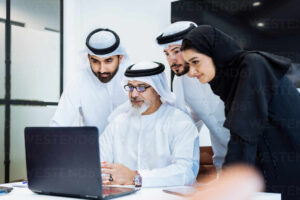group of middle eastern corporate business people wearing traditional emirati clothes meeting in the office in dubai business team working and brainstorming in the uae DMDF02230 e1710499732847